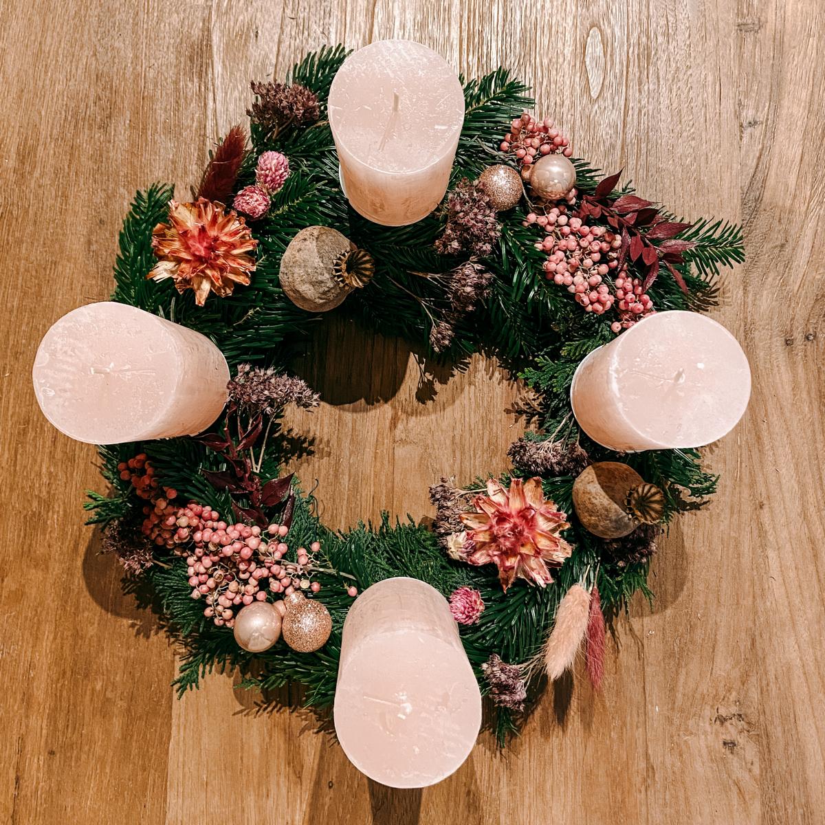 Fertiger Adventskranz mit rosa Elementen auf Holztisch – stilvolle Weihnachtsdeko Rosenrot.