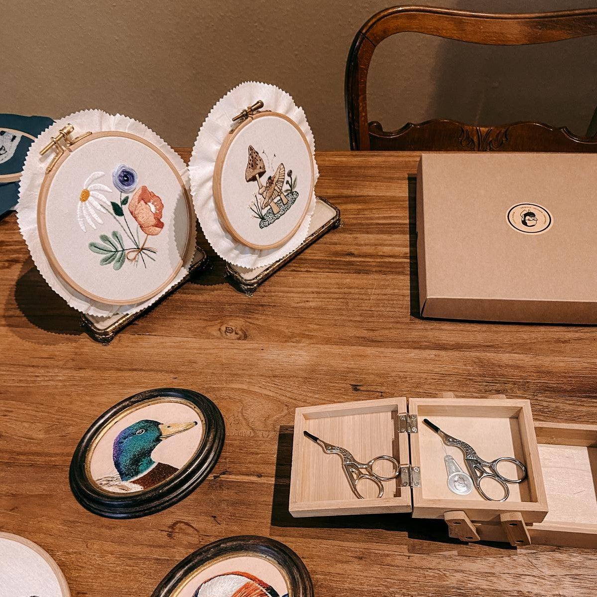 Zwei fertige Stickprojekte mit Scheren und Holzkästchen auf Tisch.