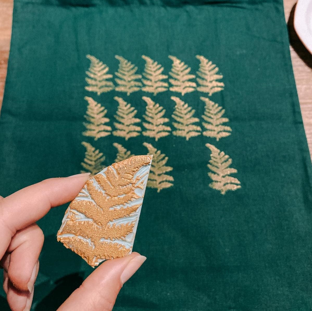 Hand hält Blatt-Stempel mit Tuch und gestempelten Blättern im Hintergrund – stempel workshop, diy druck, handmade design, auch für Firmenevents.