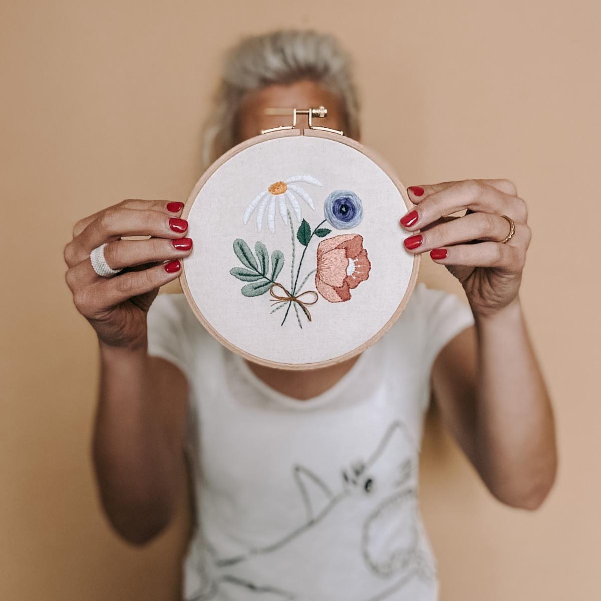 Frau hält fertige Blumen-Stickerei vor Gesicht – DIY Stickworkshop Blumenmotiv.