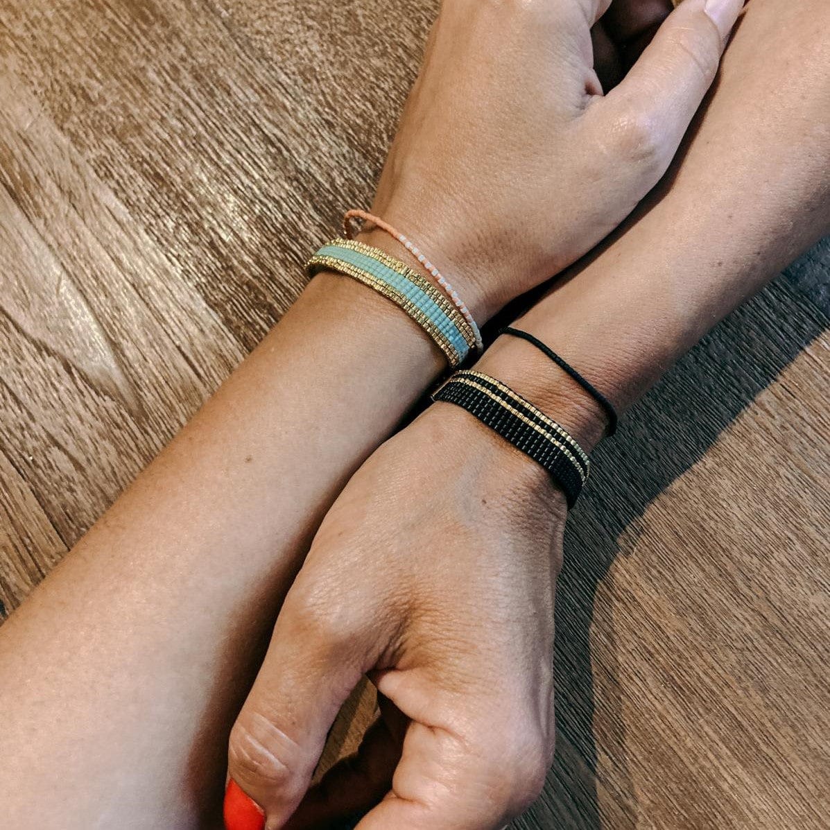 Zwei Hände halten Perlenarmbänder in verschiedenen Farbkombinationen – feiner, langlebiger Schmuck.