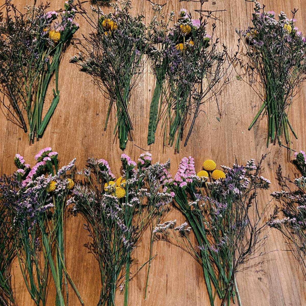 Mehrere kleine Blumensträuße auf Tisch – Materialien für Frühlingskranz Workshop, JGA-geeignet.