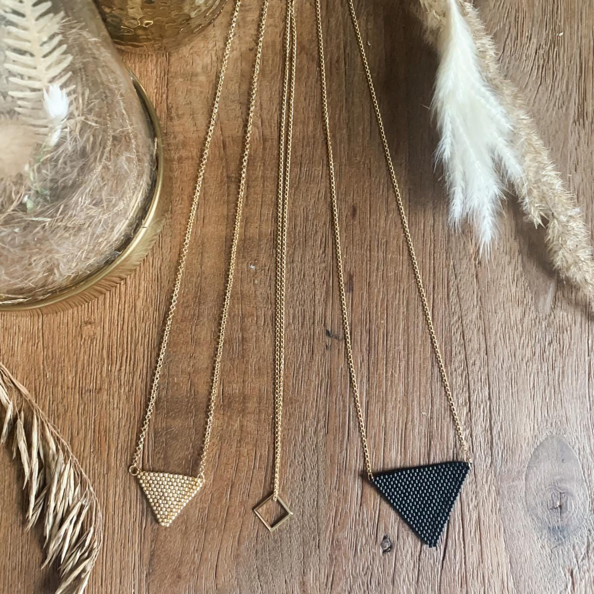 Zwei Perlenschmuck-Ketten Dreieck auf Tisch, eine in Gold, eine in Schwarz, filigraner Boho-Style Modeschmuck.