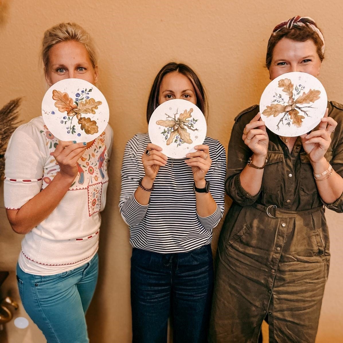 Drei Teilnehmer halten ihre fertigen Herbst-Aquarellbilder vor das Gesicht – Workshop für Anfänger.