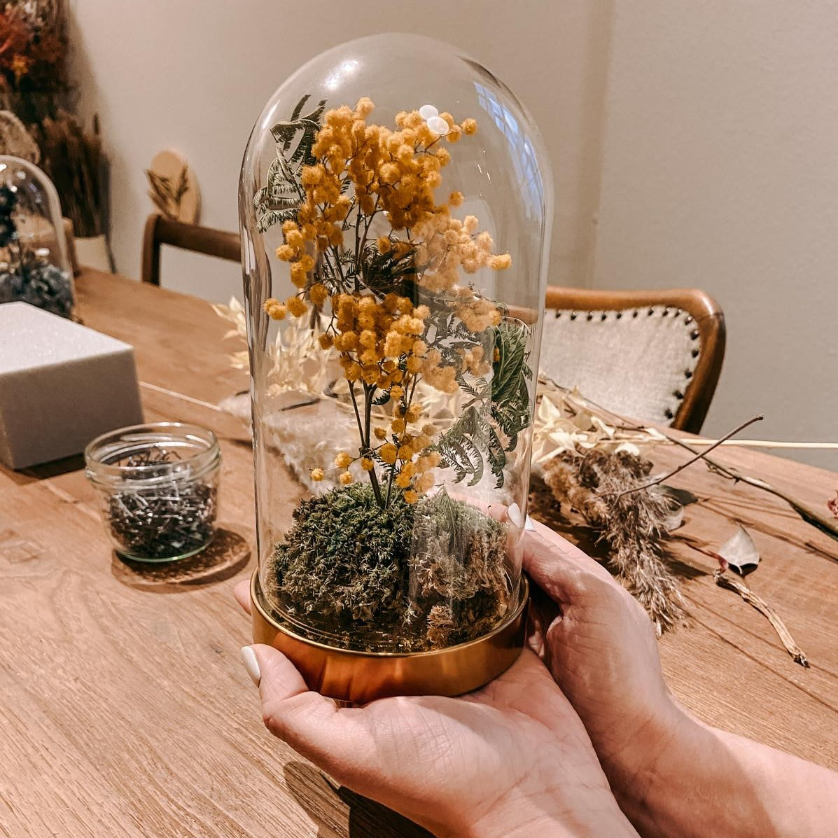 Zwei Hände halten fertige Glasglocke mit gelben Trockenblumen – Boho Style Home Deko.