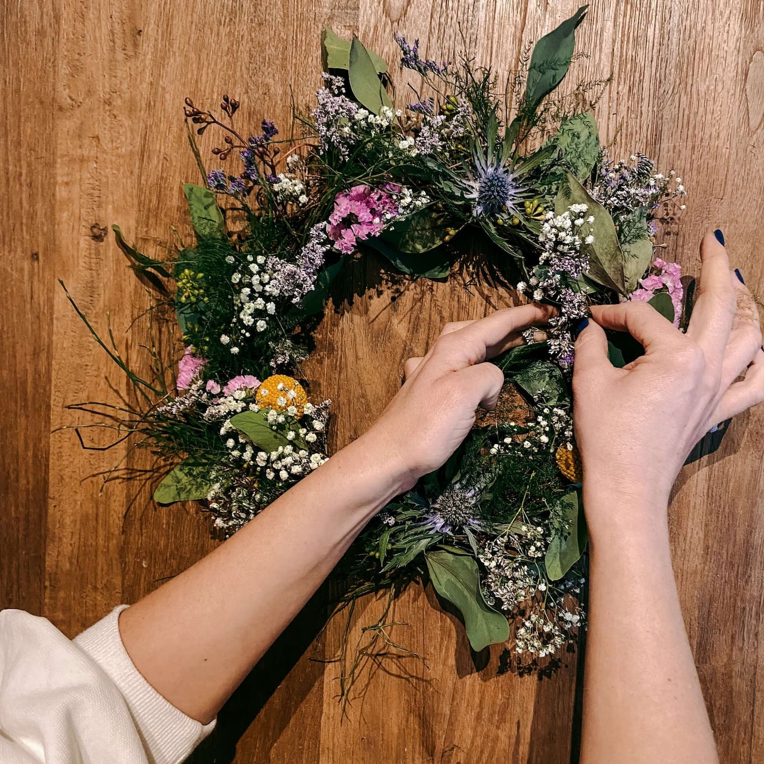 Fast fertiger Kranz mit bunten Blumen von zwei Händen bearbeitet – Workshop JGA & Team.
