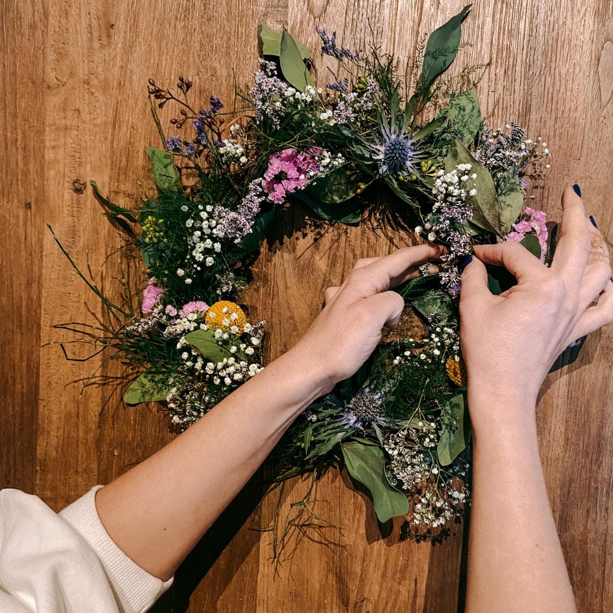 Hände binden bunte Blumen an Kranz – kreative DIY Bastelarbeit für Frühlingsdekoration.