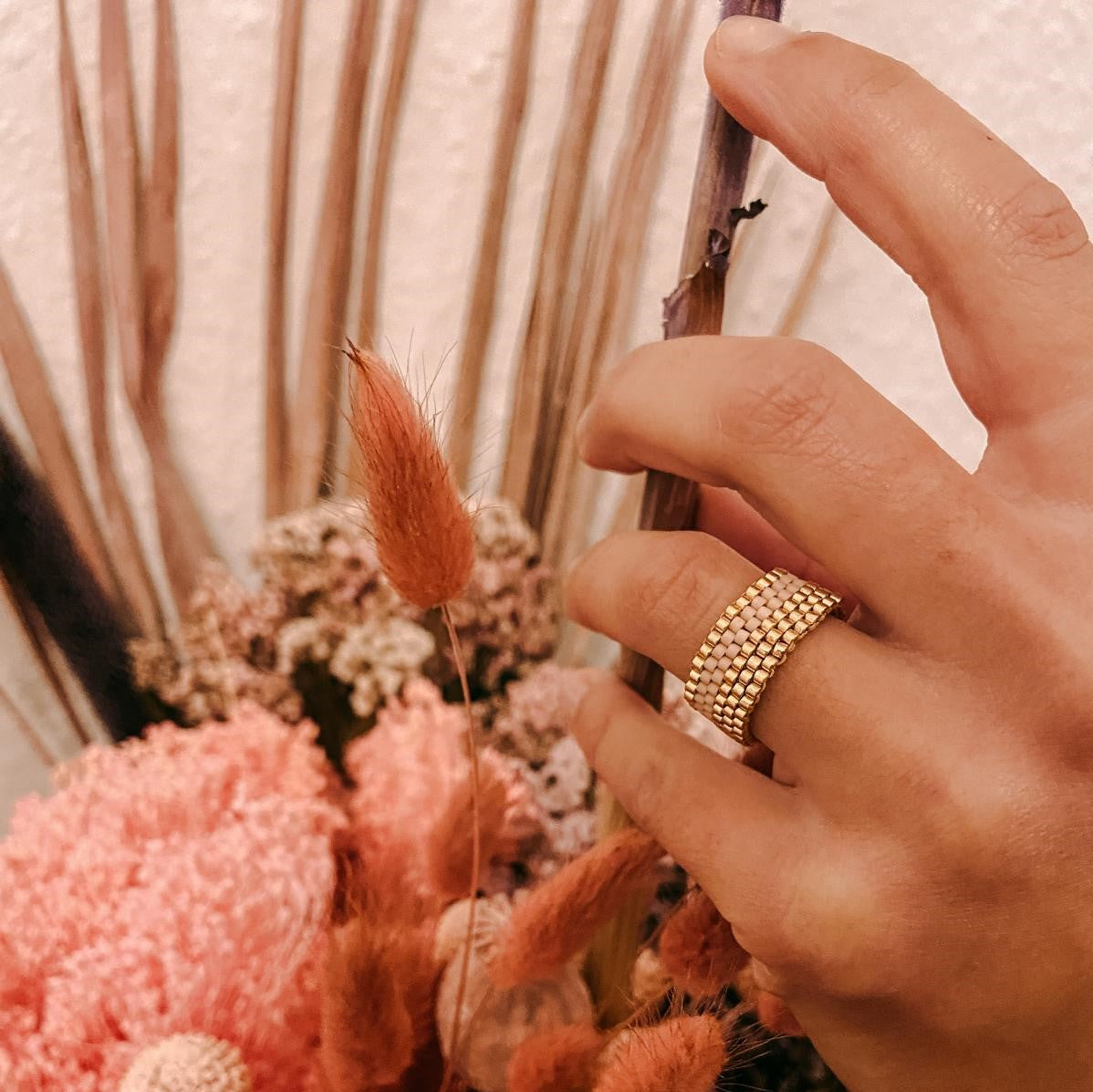 Hand hält goldenen Perlenring an Trockenblumen, Nahaufnahme – Miyuki Perlenring, DIY Schmuck