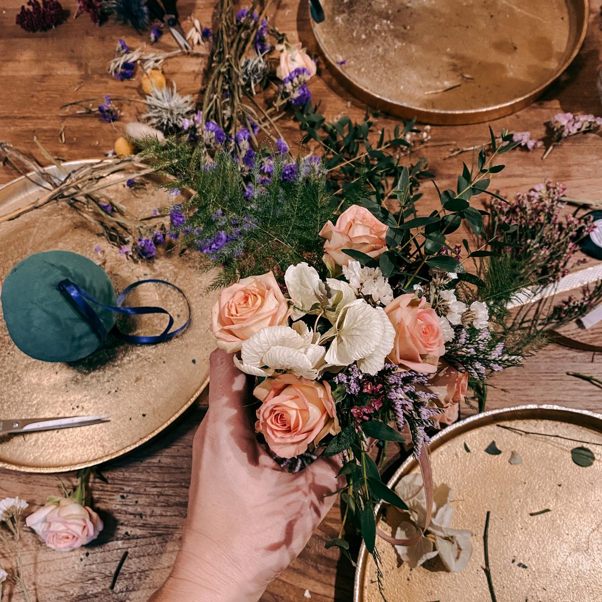 Hand hält FlowerBall, im Hintergrund Blumen, Schere und Tabletts – DIY Workshop für frische Blumenarrangements.