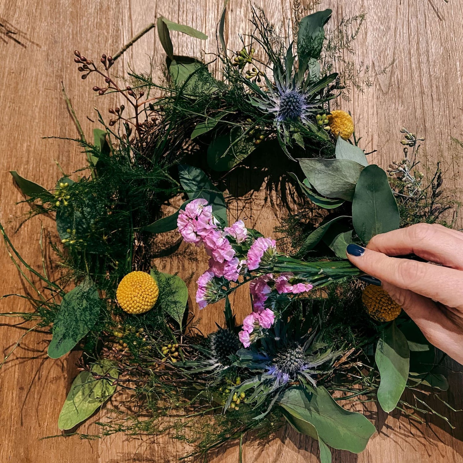 Hand hält pinke Blumen vor Kranz – Workshop DIY Frühlingskranz als Teamevent oder JGA.