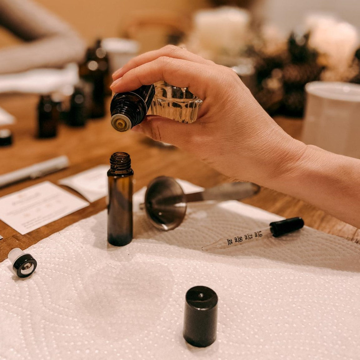 Hand füllt kleine Flasche mit Öl, Papiertuch darunter – naturparfum kurs, parfum selber machen, nachhaltige kosmetik, auch für Firmenevents.