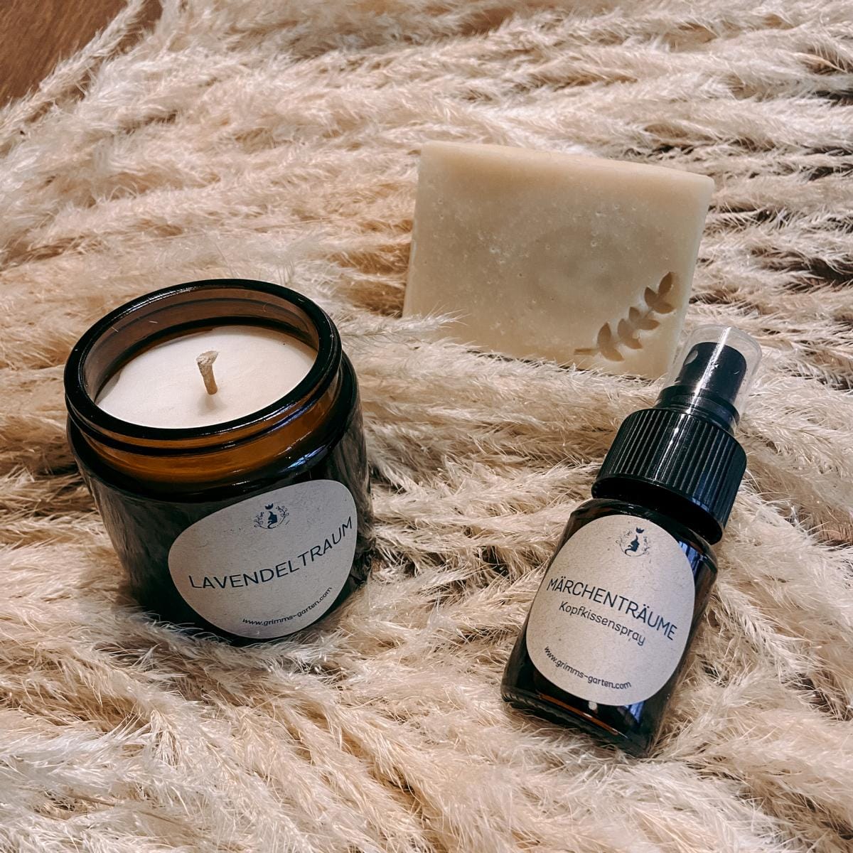 Geschenkset Lavendel unverpackt: Duftkerze, Kopfkissenspray und Lavendelseife auf Tisch dekoriert mit Lavendelblüten.