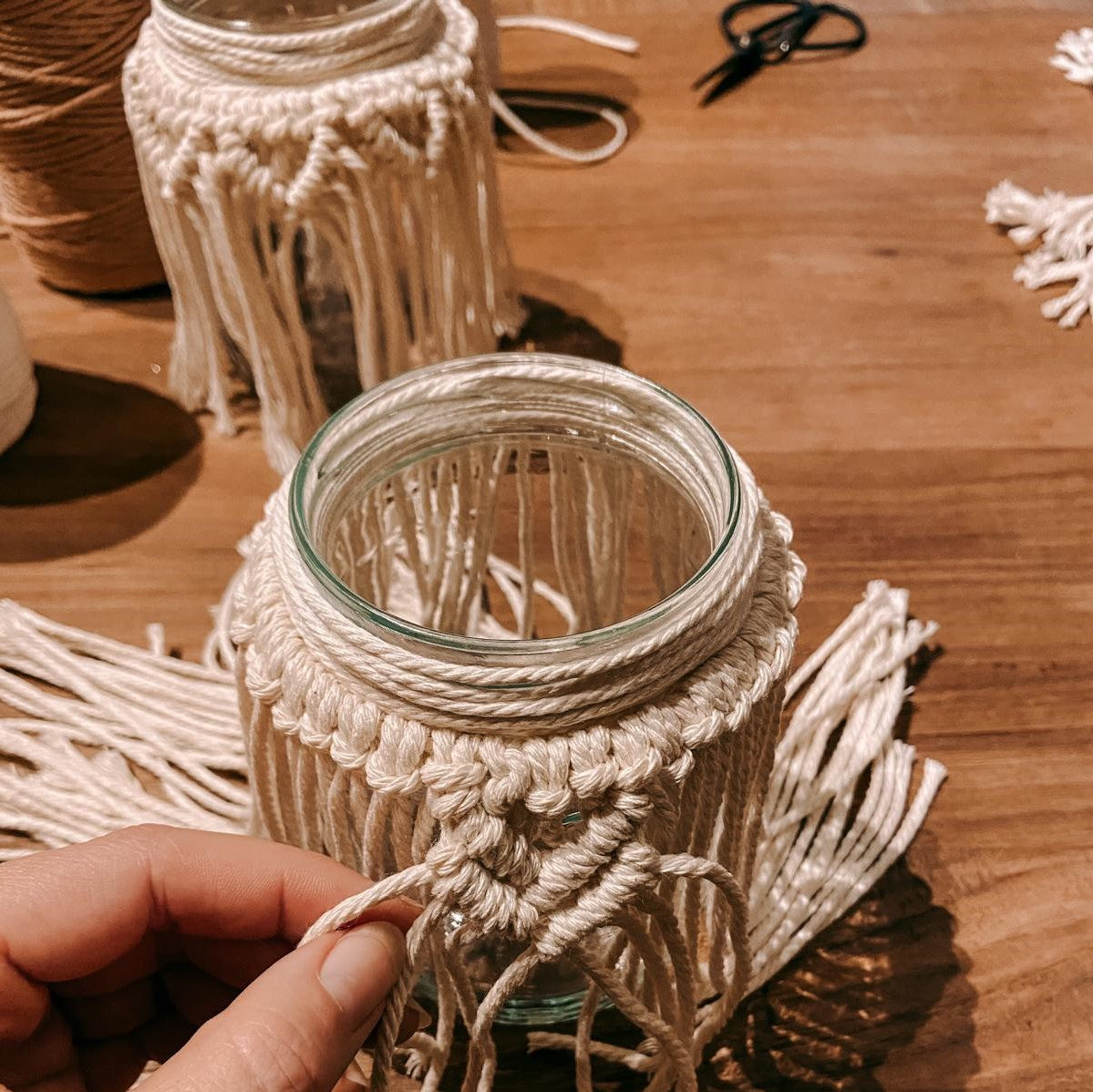 Hand hält fertiges Makramee an Glas – kreative Boho Dekoration zum Selbermachen.