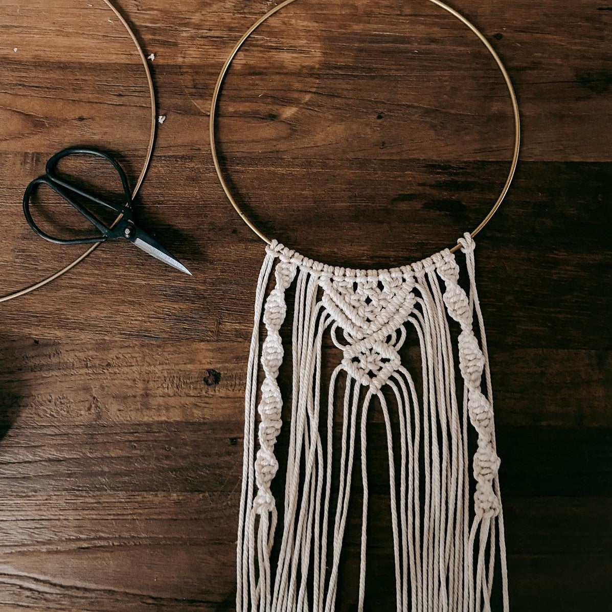 Halbfertiger Makramee Ring auf Tisch mit Schere, DIY Wandbehang in Arbeit.