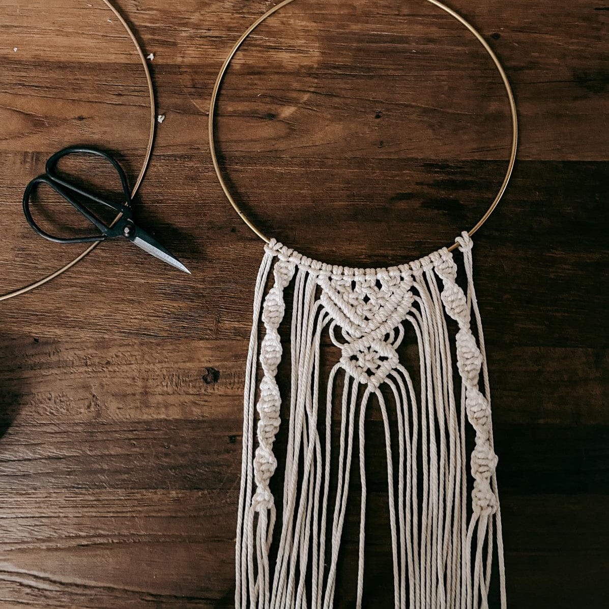 Halbfertiger Makramee Ring auf Tisch mit Schere, DIY Wandbehang in Arbeit.