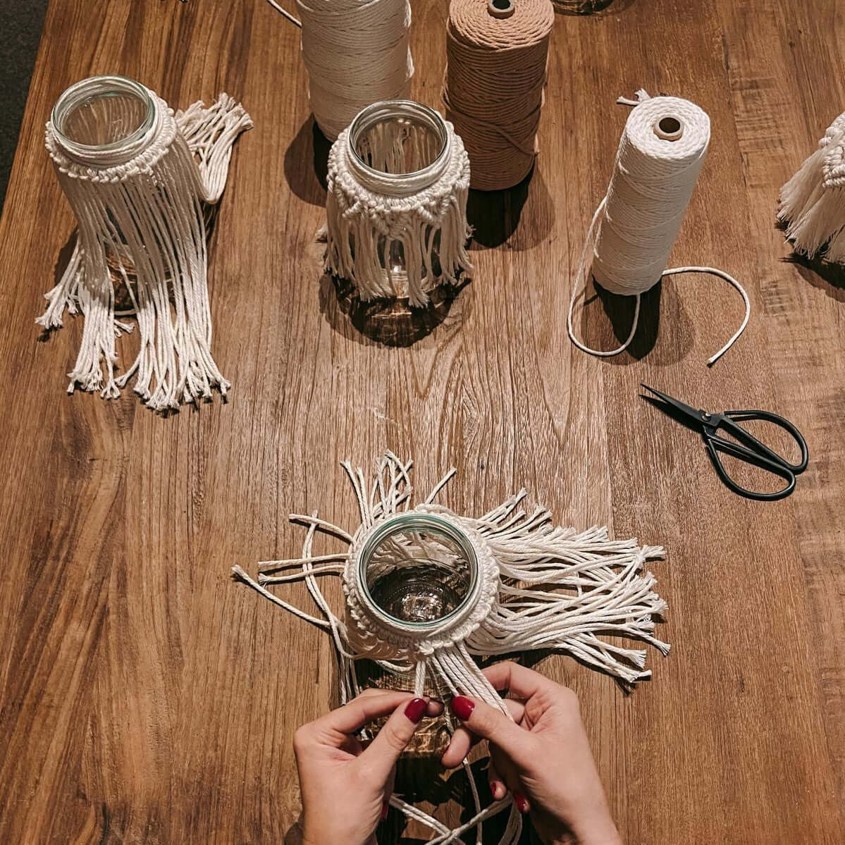 Hand knüpft Makramee mit fertigen Gläsern im Hintergrund – Boho Lichtglas Workshop in Berlin