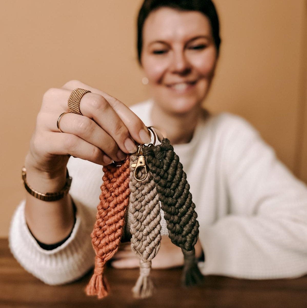 Person hält drei Makramee Anhänger in Orange, Beige und Grün in der Hand, handgemachter Schlüsselanhänger.