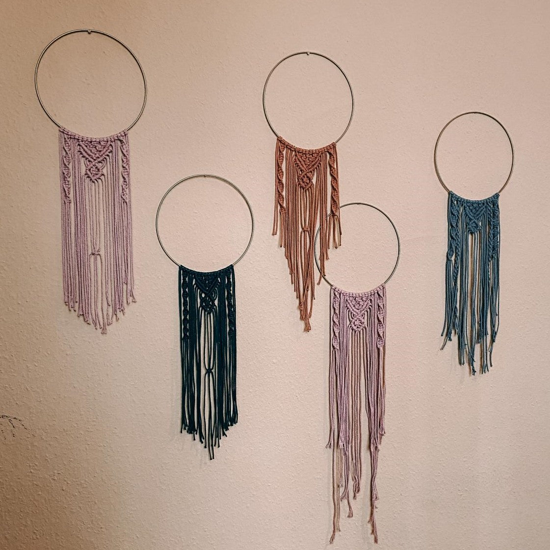 Fünf fertige Makramee-Ringe in verschiedenen Farben hängen an der Wand – Boho Style, Makramee Wanddeko, kreative Handarbeit.