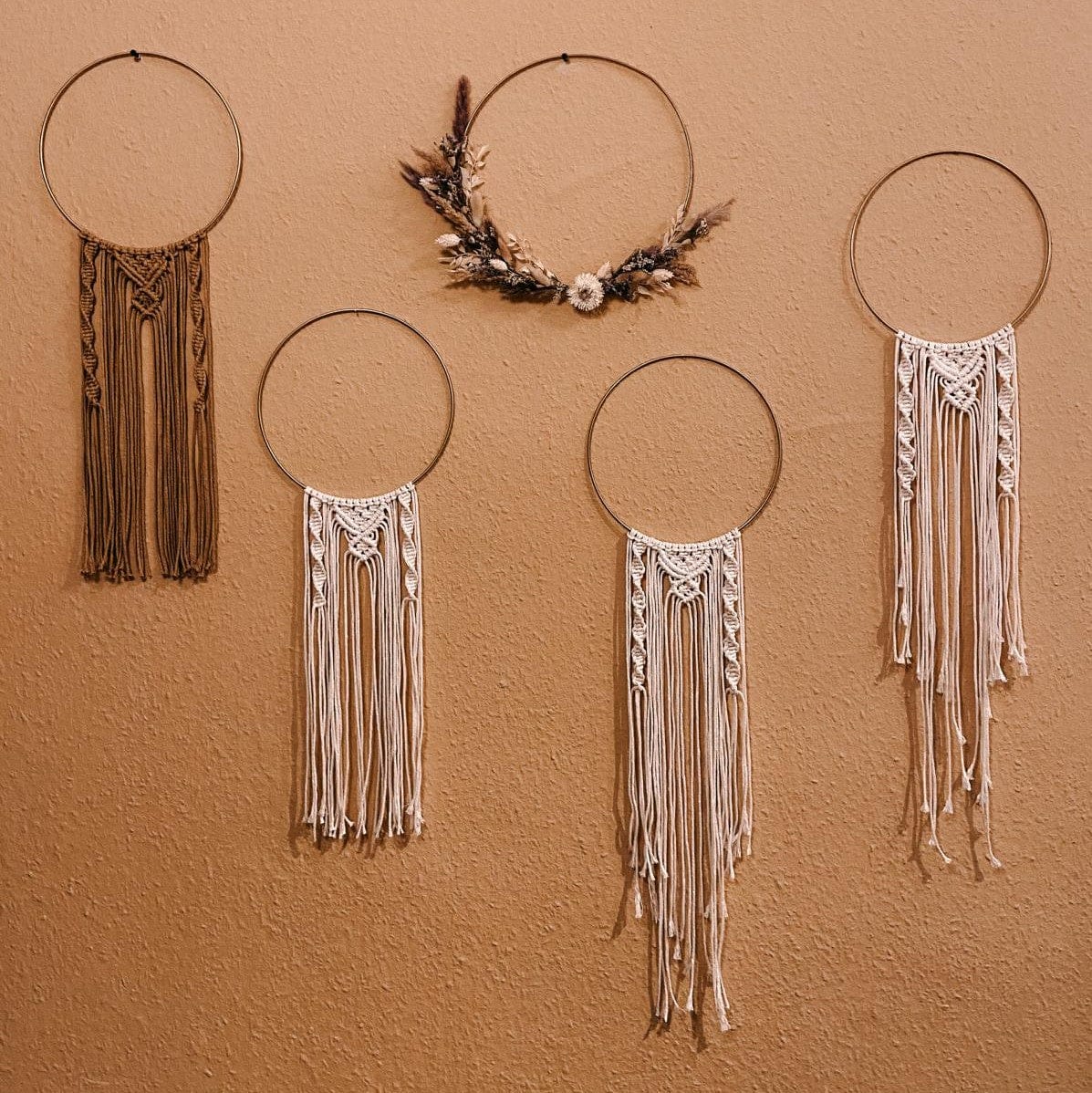 Vier Makramee-Ringe in unterschiedlichen Farben und Formen hängen an der Wand – Interior Design Boho, Makramee Kunst.