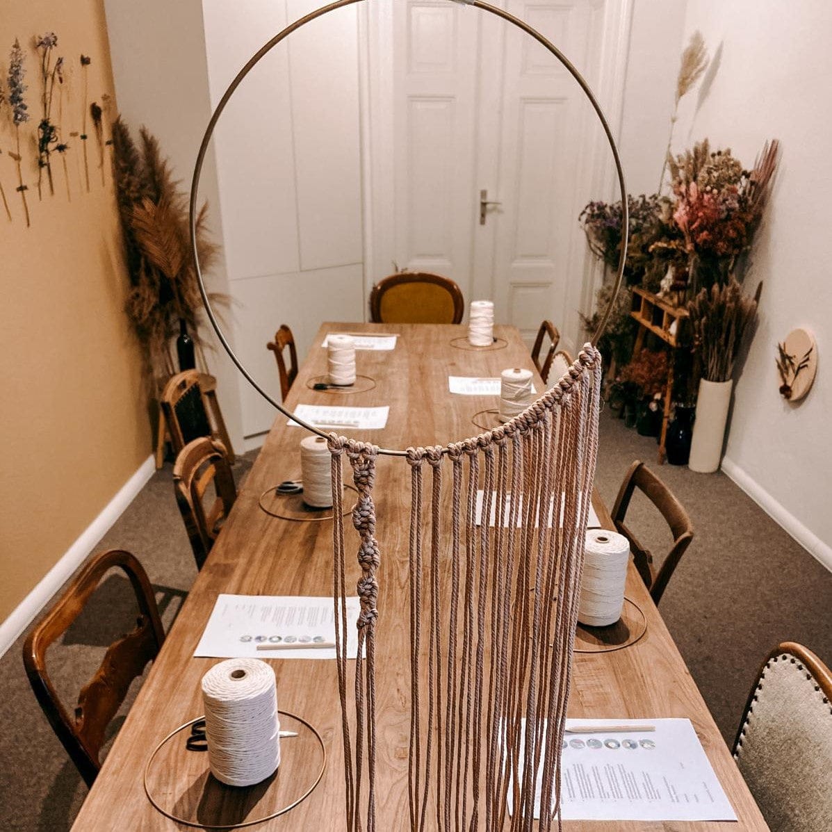 Halbfertiger Makramee-Ring in der Luft vor dem Tisch – DIY Boho Ring, Handarbeit in Aktion, Makramee Technik.