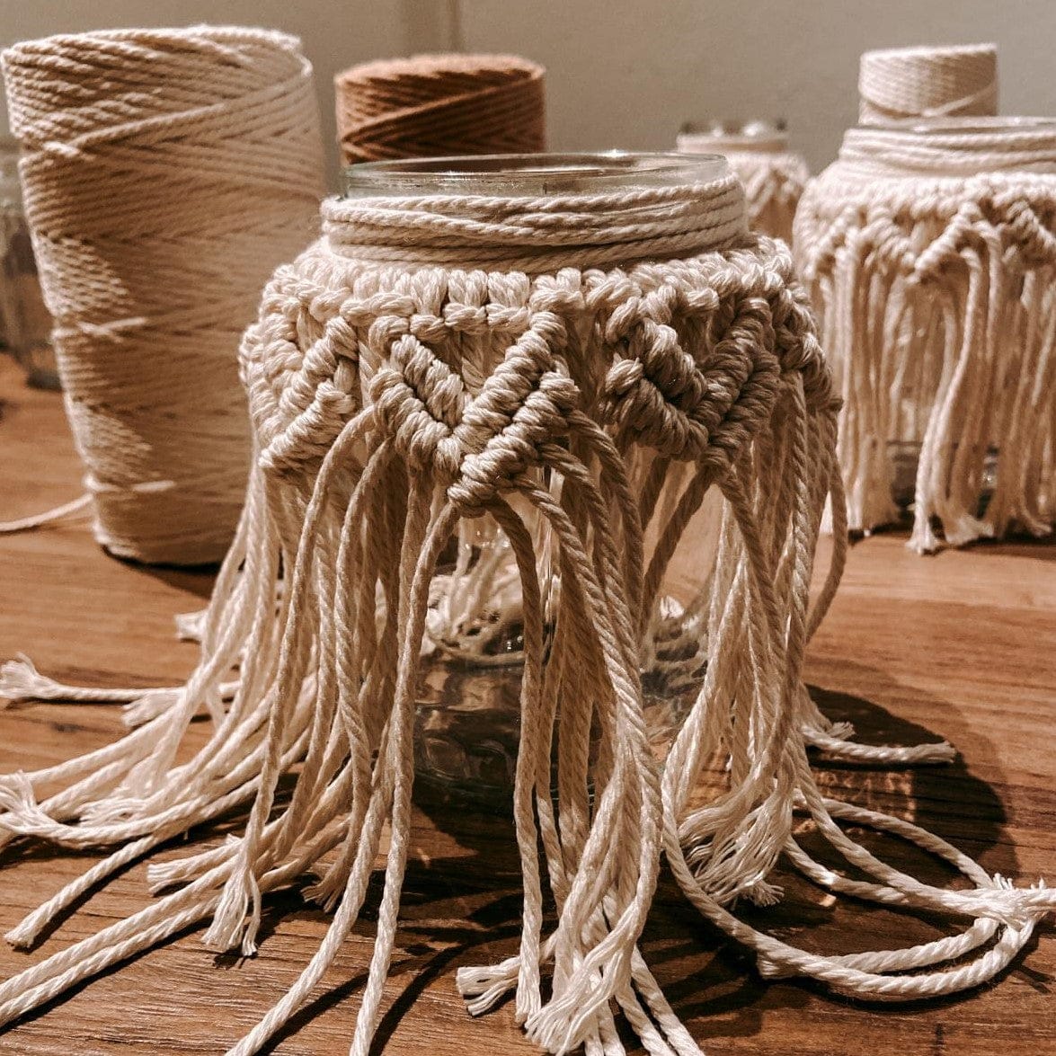 Zwei fertige Makramee Gläser mit Garn auf Holztisch – Boho Dekoration im DIY Workshop Berlin.