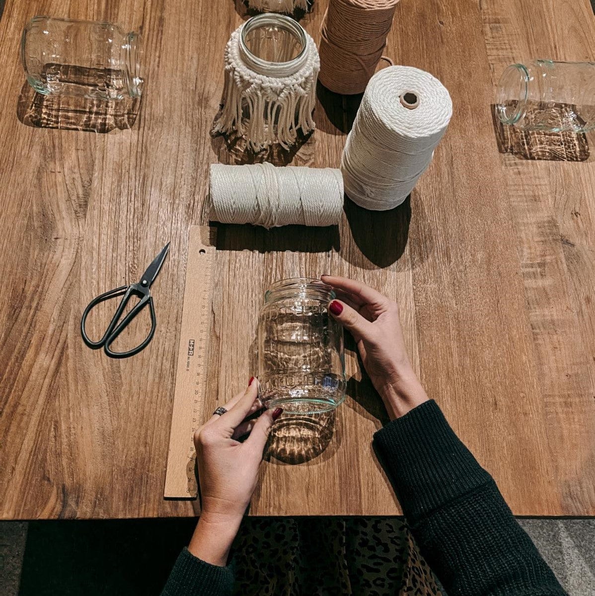 Hand hält Glas mit Garn und Schere – Makramee Licht Workshop für stilvolle Boho Dekoration.