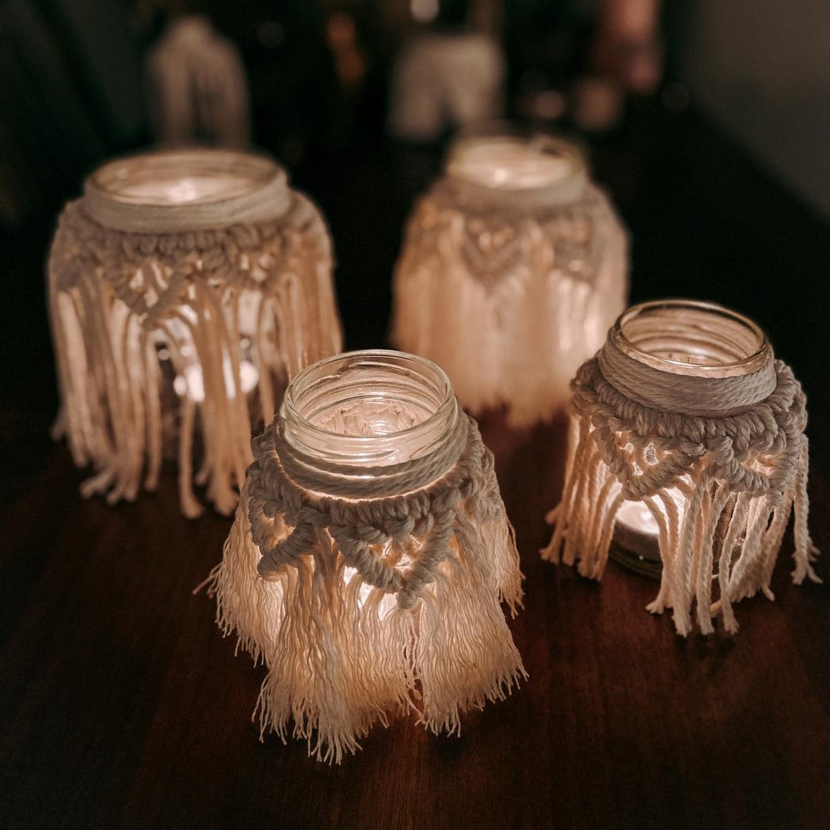Vier fertige Makramee-Teelichter auf Tisch, die leuchten – DIY Boho Workshop.