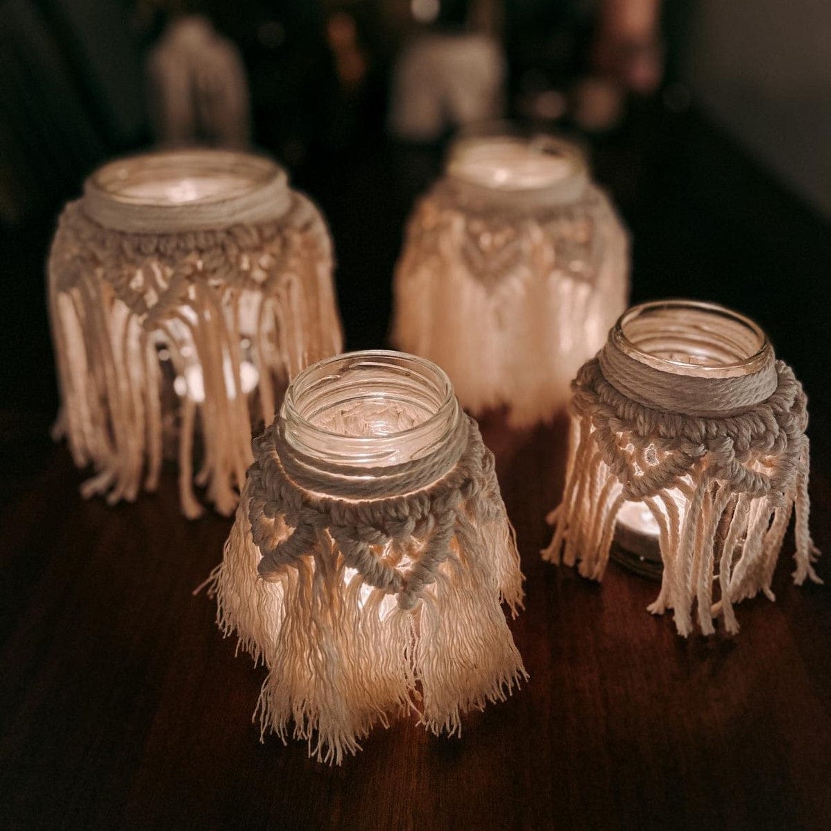Vier fertige Makramee-Teelichter auf Tisch, die leuchten – DIY Boho Workshop.
