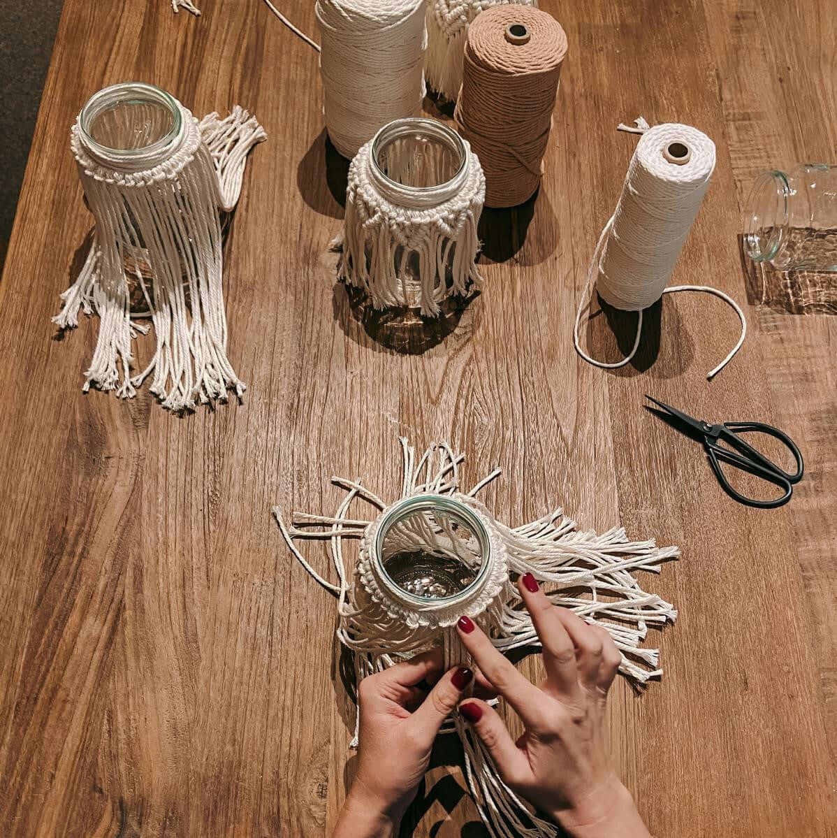 Makramee-Gläser auf Tisch mit Garn und Materialien – Boho DIY Workshop.