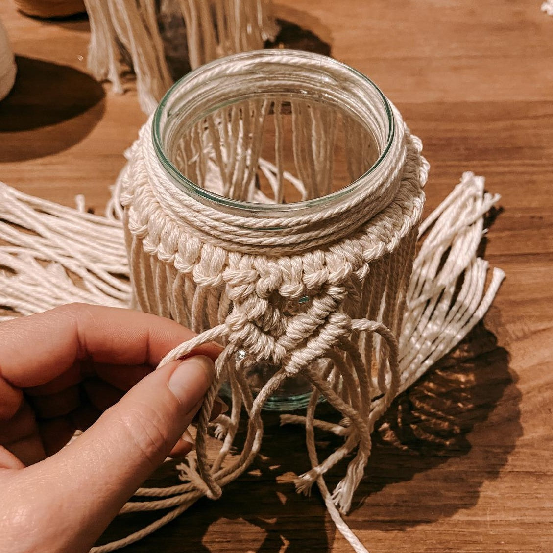 Hand hält Glas mit Makramee Muster – DIY Boho Makramee Licht aus Garn selbst gestalten.