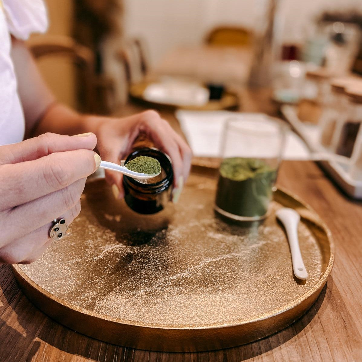 Zwei Hände entnehmen grünes Pulver aus Glas mit Löffel – Naturkosmetik Workshop.