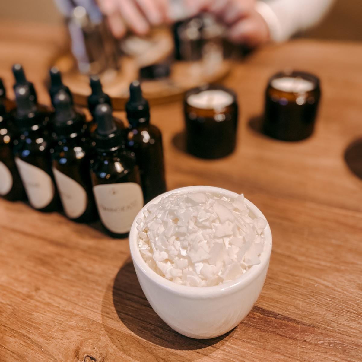 Behälter mit Kerzenwachschips, viele Duftfläschchen dahinter – DIY Kerzen Workshop, auch für Firmen.