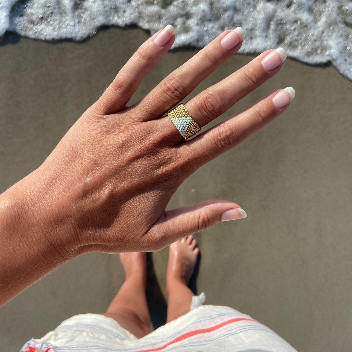 Hand trägt stilvollen Perlenring aus goldfarbenen Miyuki-Perlen am Finger.