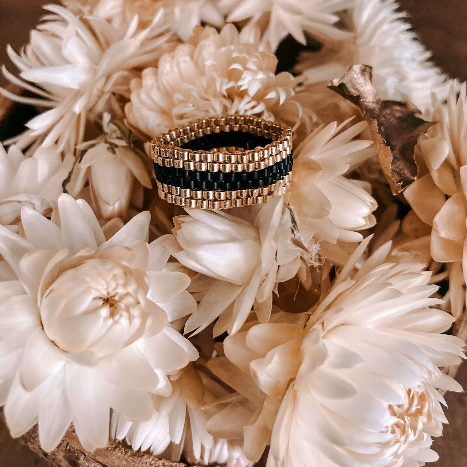 Gold-schwarzer Perlenring Nahaufnahme auf weißen Blumen – DIY Perlenring, japanische Glasperlen