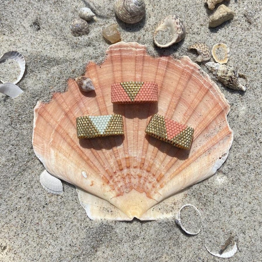 Perlenring aus goldfarbenen Miyuki-Perlen in Peyote-Technik auf Muschel im Sand präsentiert.