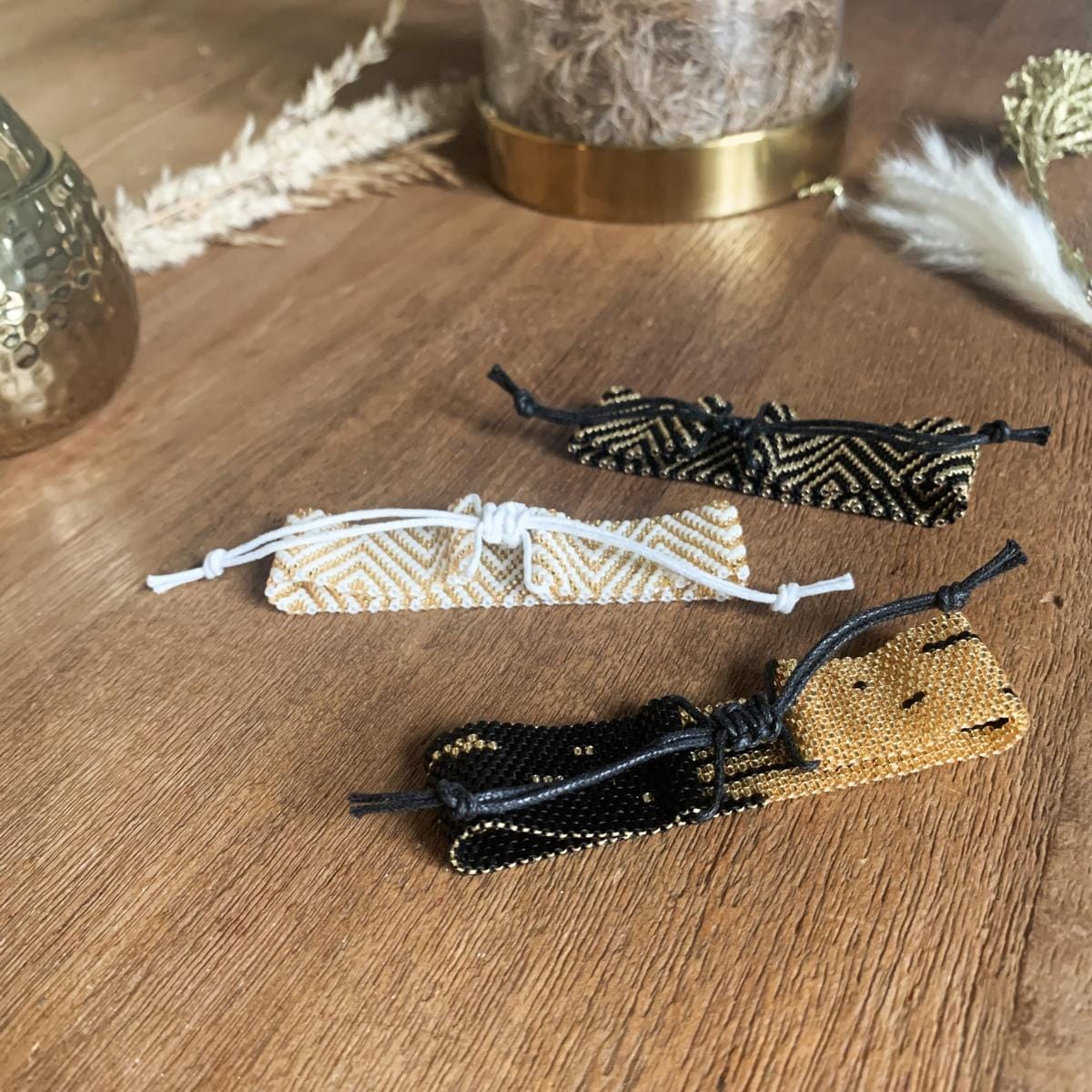 Drei handgefertigte Perlenschmuck Armbänder in Gold, Schwarz und Weiß auf Tisch dekorativ arrangiert.
