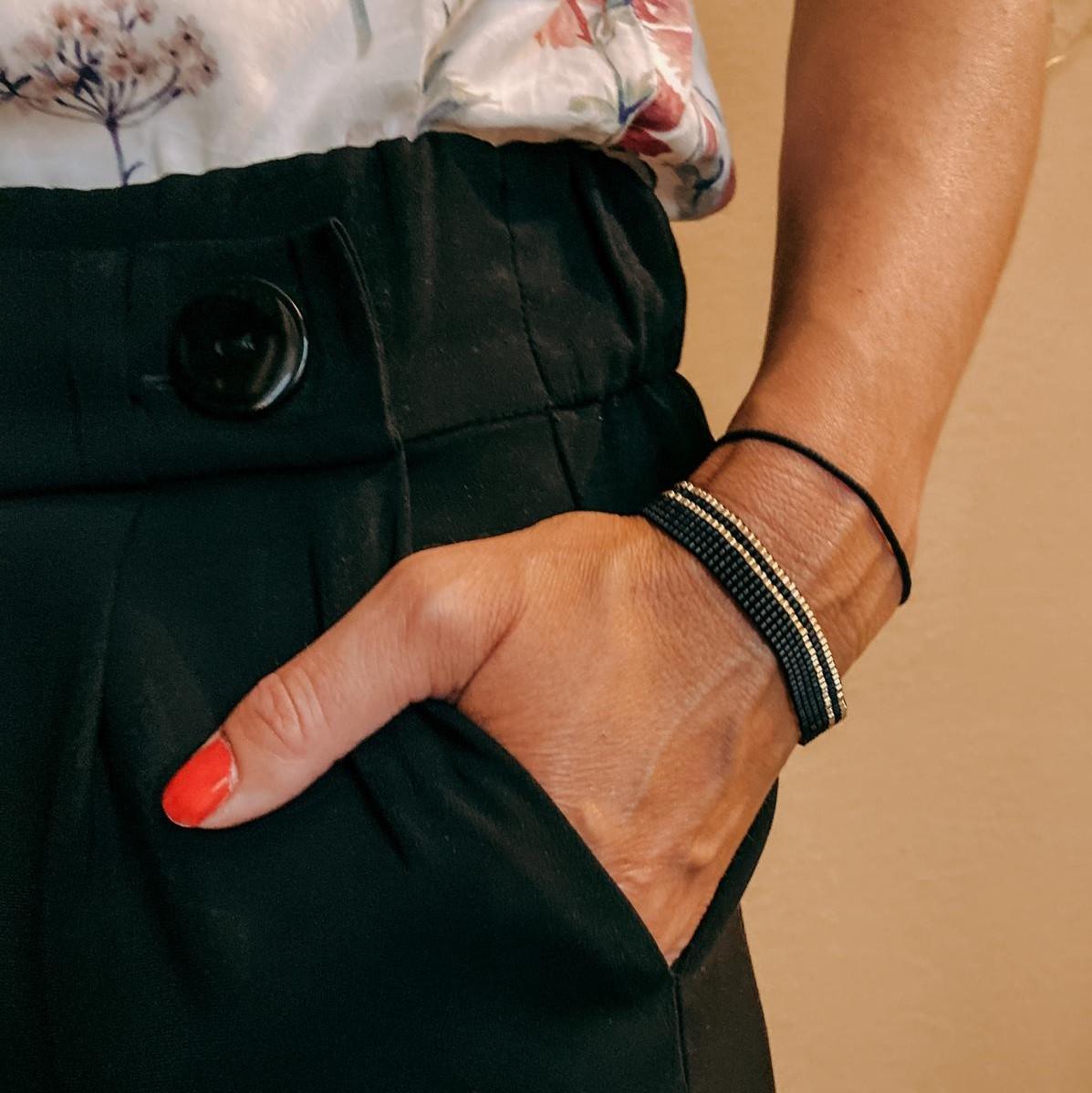 Hand trägt ein handgefertigtes Perlenschmuck-Armband in Schwarz-Gold aus japanischen Miyukiperlen, Boho-Style.