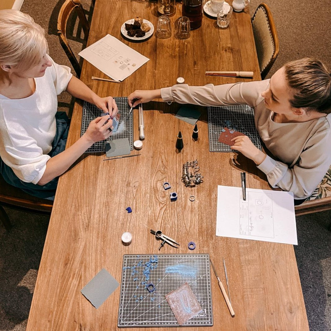 Zwei Personen sitzen gegenüber und arbeiten an Ringen – DIY Ring Workshop, Schmuckdesign, Handarbeit.