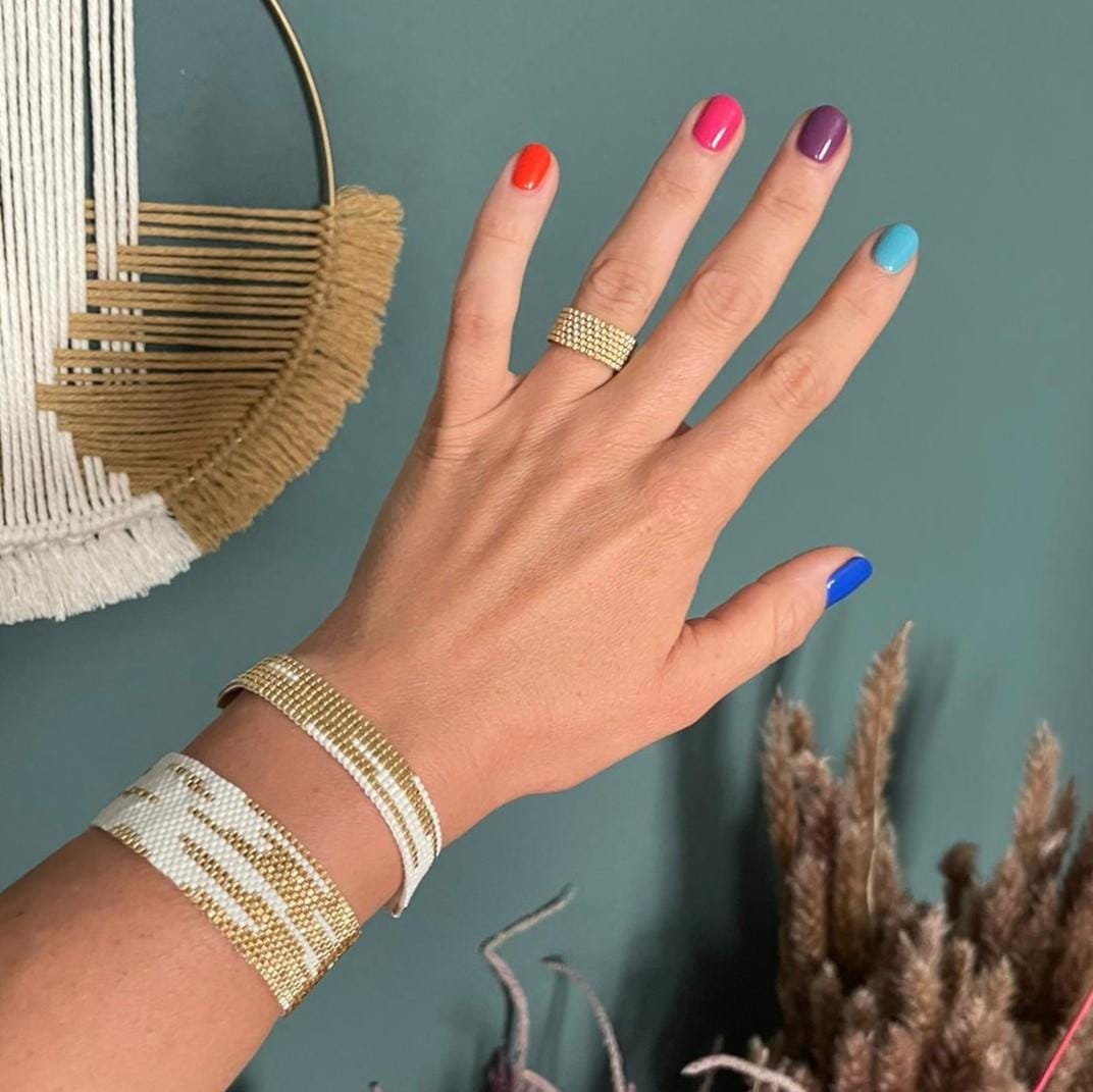Hand trägt zwei Perlenschmuck-Armbänder in Gold und Weiß – eleganter Boho-Schmuck.