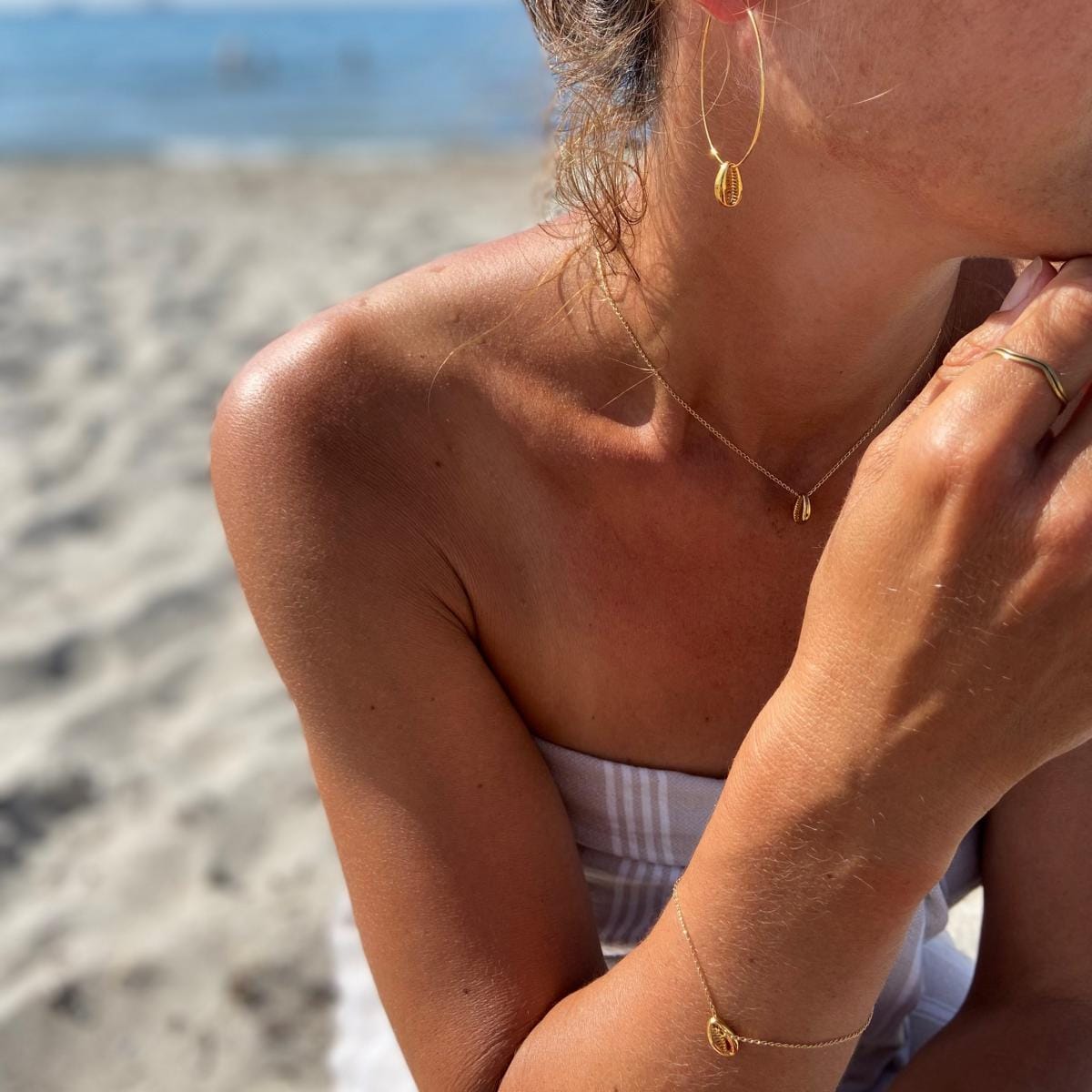 Frau trägt Kauri-Muschel Creolen und passende Kette am Strand, sommerlicher Schmuck-Look.