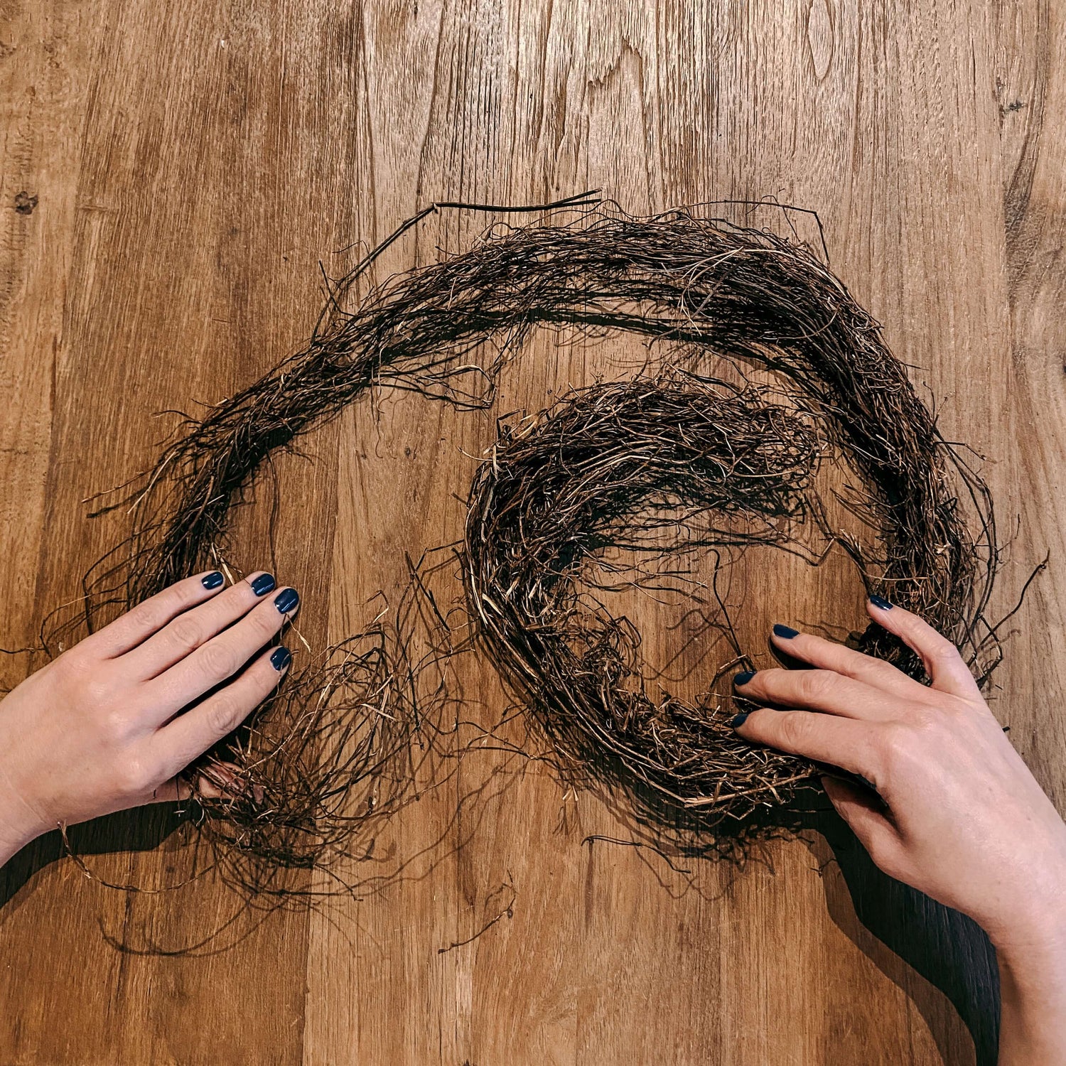 Zwei Hände formen braune Zweige auf Tisch – Frühlingskranz Workshop für JGA & Team.