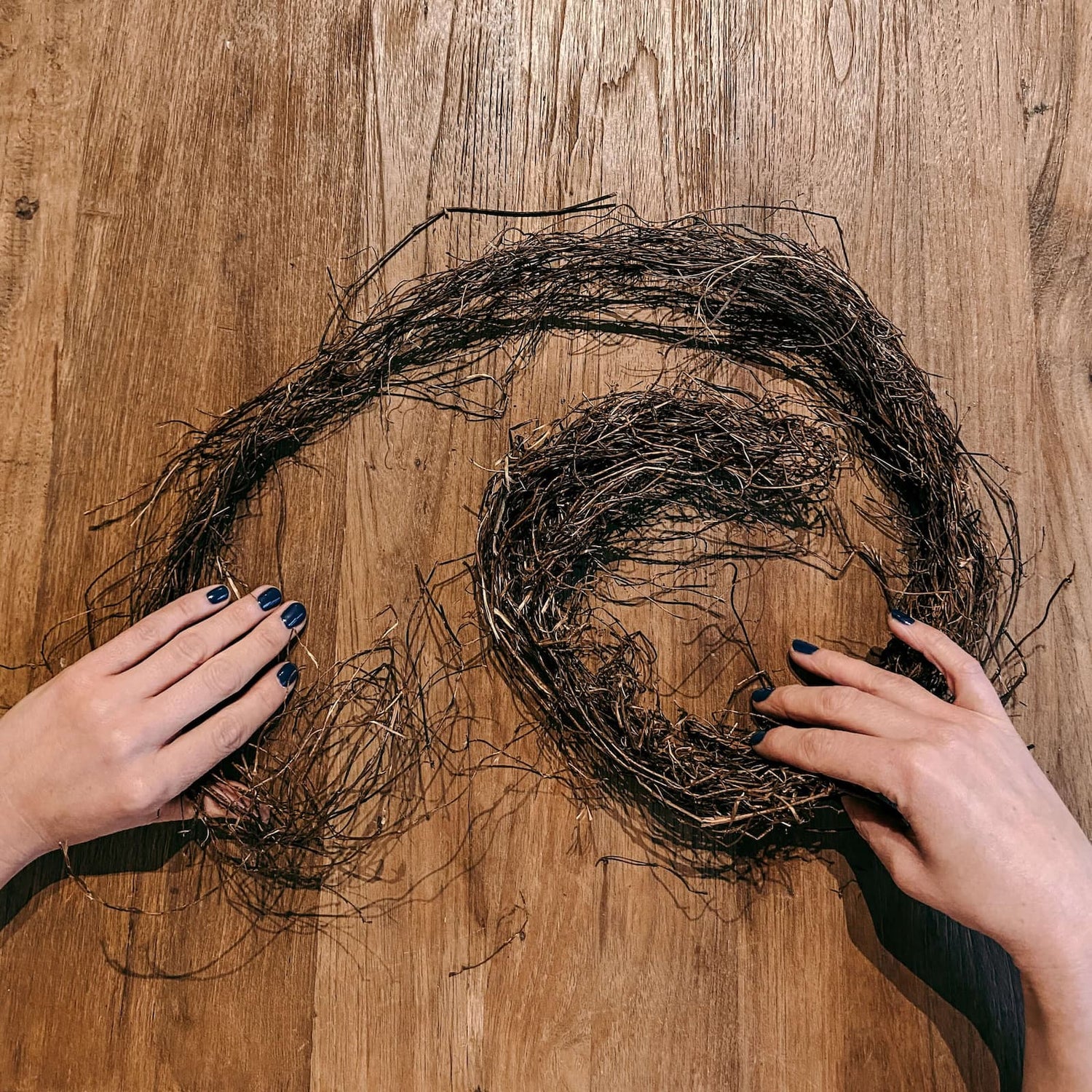 Zwei Hände formen braune Zweige auf Tisch – Frühlingskranz Workshop für JGA & Team.