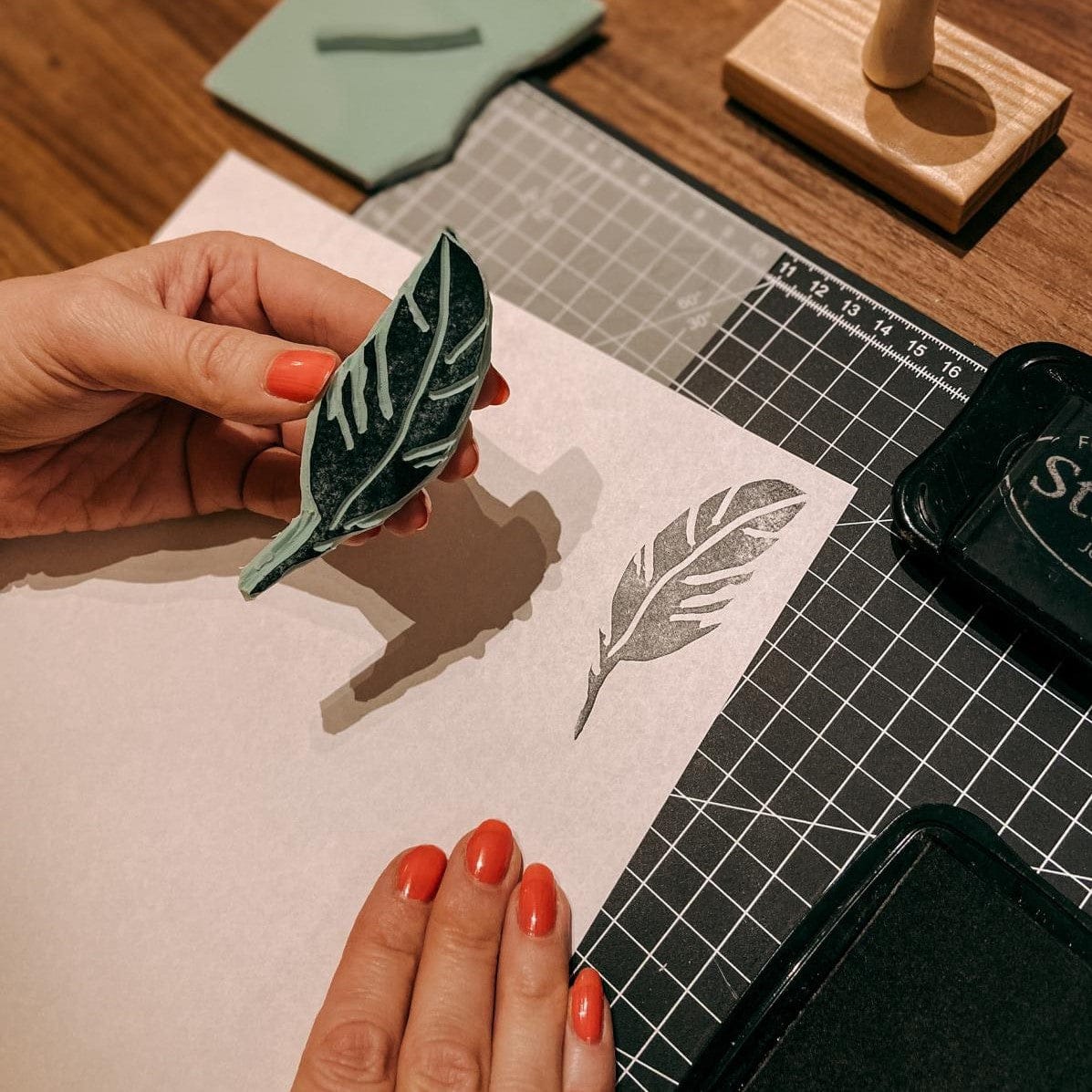 Hand hält Blatt-Stempel auf Schnitzmatte, gestempelte Blätter daneben – stempel workshop berlin, diy textildruck, auch für Firmenevents.