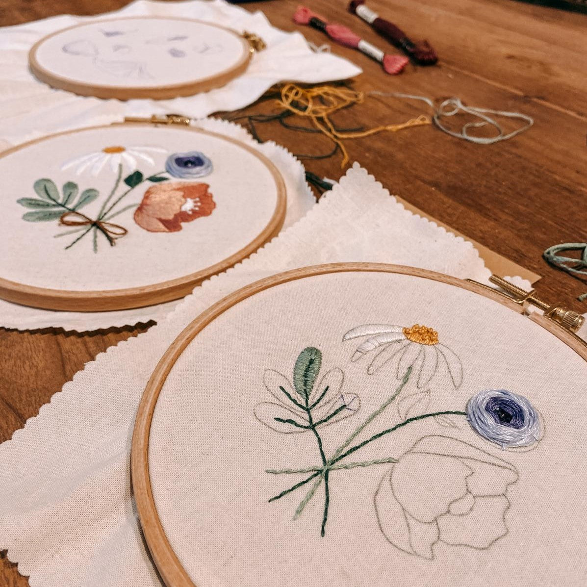 Angefangene Stickerei liegt neben fertigem Blumenmotiv auf Tisch.