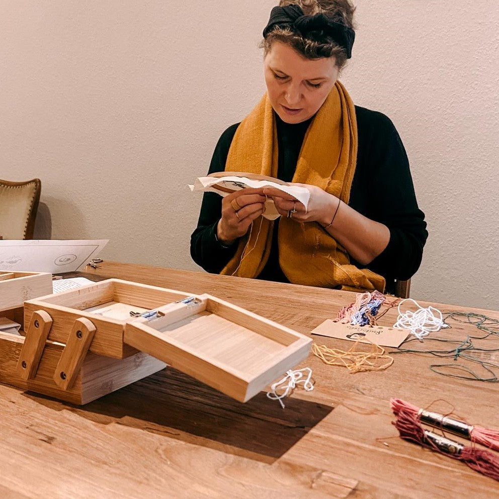 Frau stickt Pilzmotiv auf Stoff mit Garn auf Tisch – kreative Stickerei.