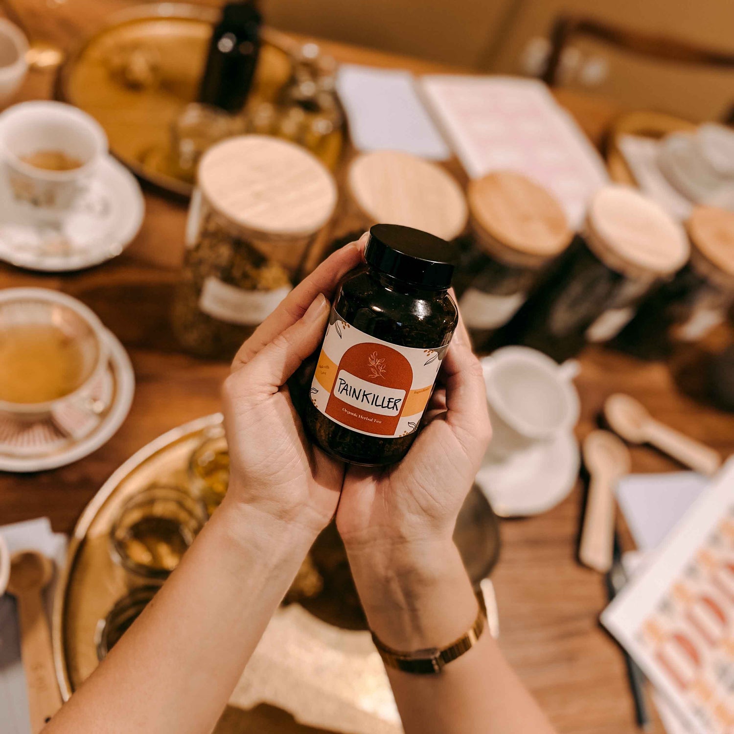 Zwei Hände halten geschlossenes Glas „Painkiller“ – kräutertee workshop, DIY Tee, Teamevent.