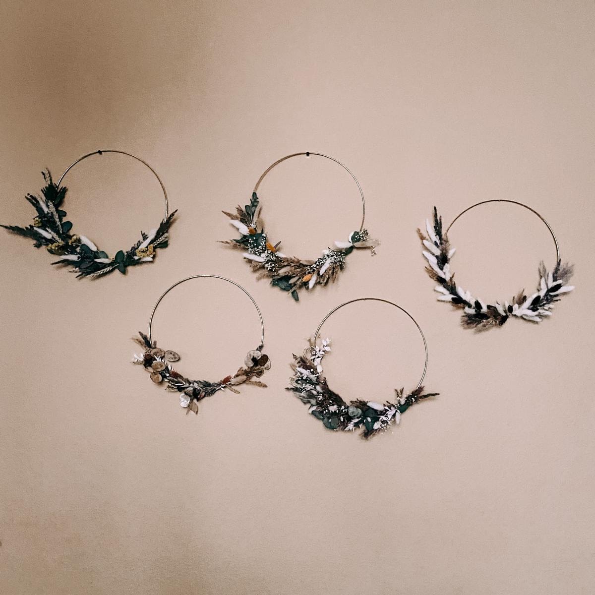 Fünf fertige Trockenblumenringe hängen an Wand in verschiedenen Farben – Boho-Deko DIY Workshop.