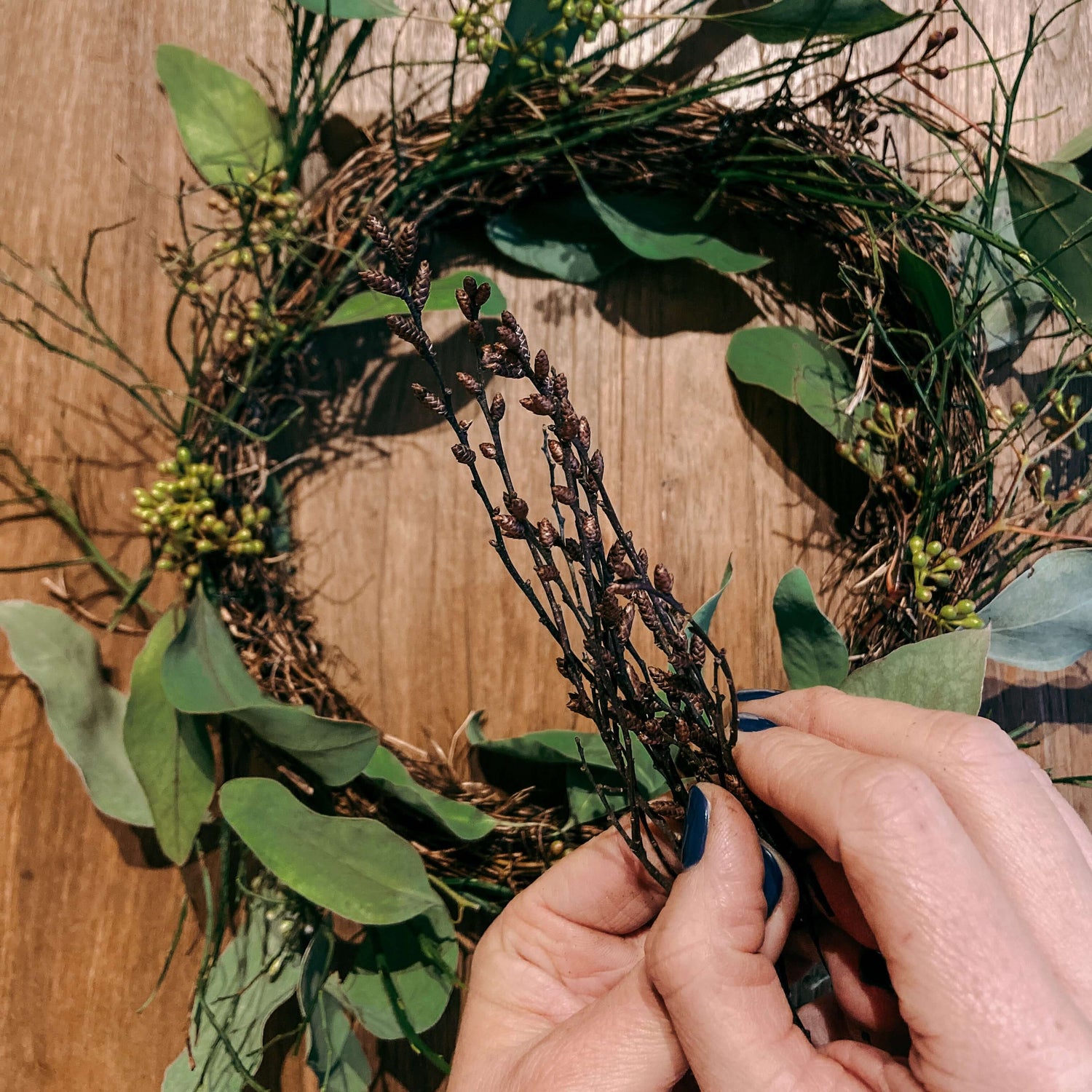 Hände halten kleine Zweige vor grünem Kranz im Hintergrund – Team- oder JGA-Workshop.