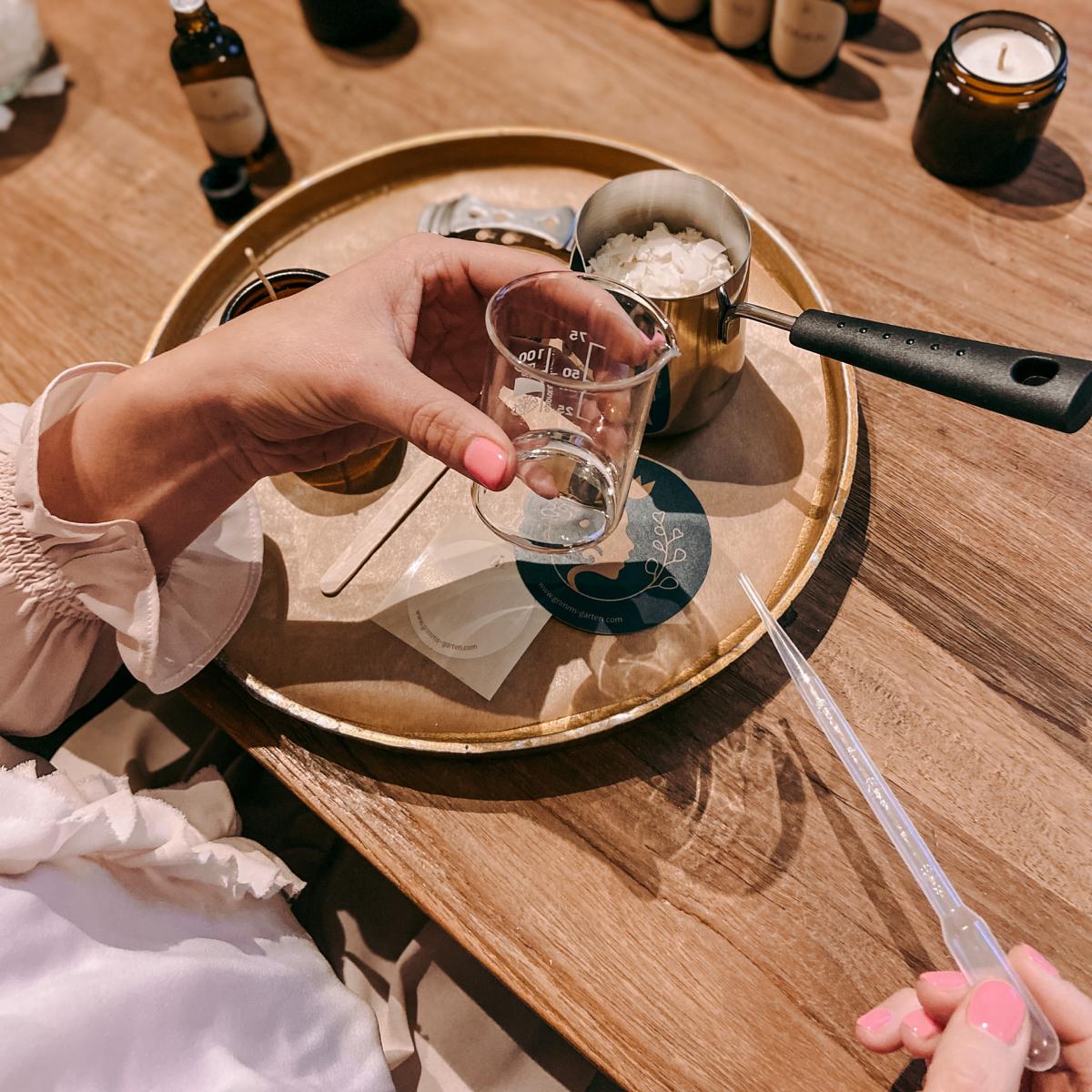 Hand hält Pipette, andere Hand Glasgefäß – Materialien für DIY Duftkerze, Workshop auch für Firmen.