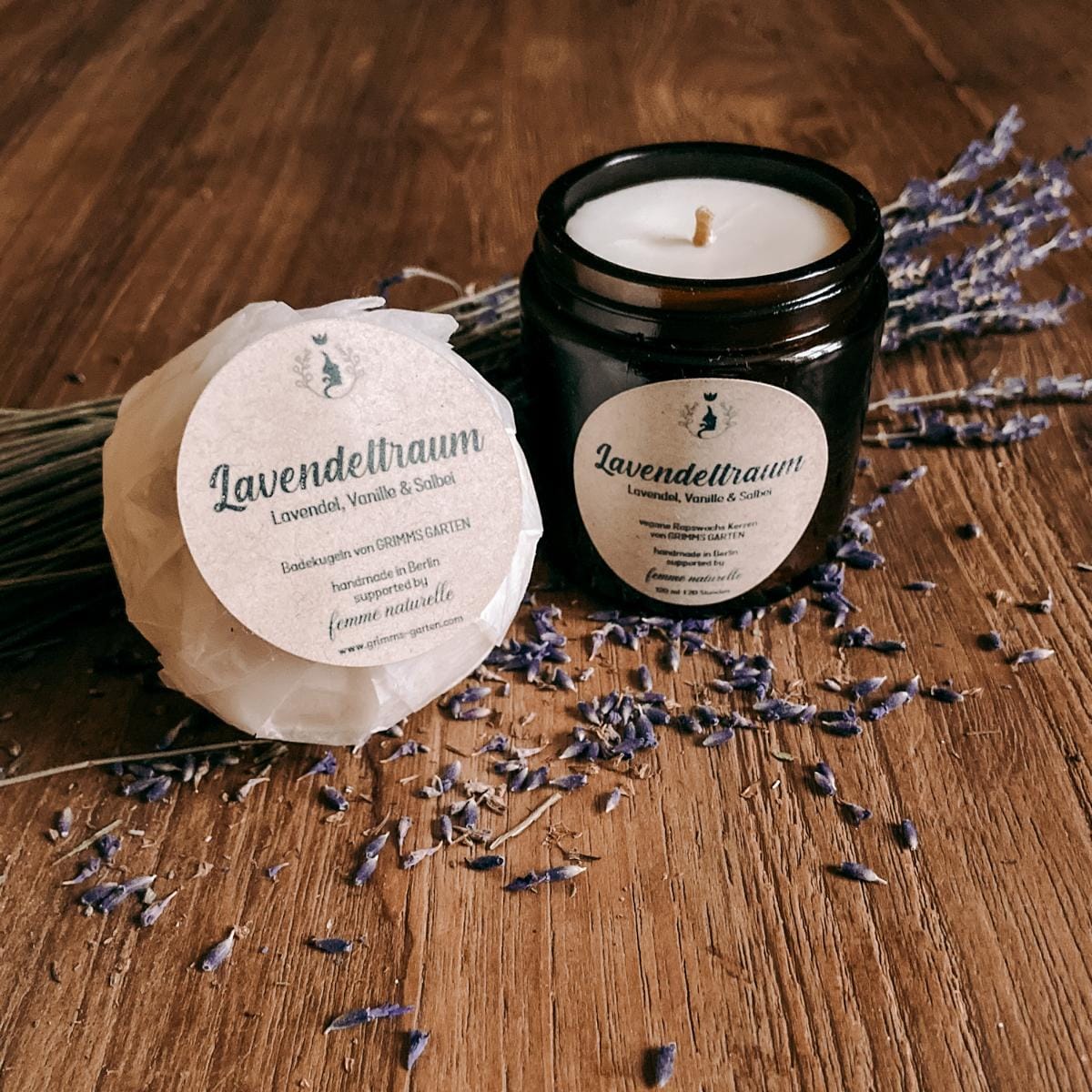 Wohlfühlset Lavendeltraum mit veganer Duftkerze und Badekugel vor Lavendelblüten auf Holztisch.